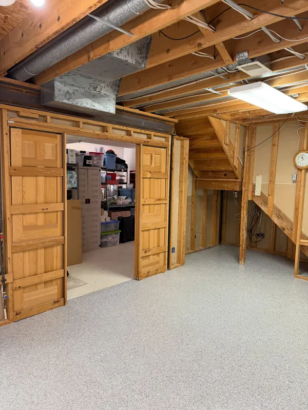 Basement with a light gray flake floor coating, exposed ceiling joists and wood double doors open to a storage room