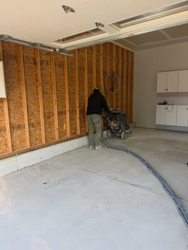 Installer diamond grinding a bare garage floor next to unfinished stud walls