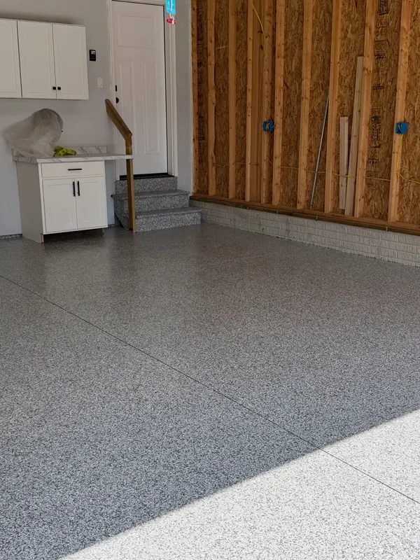 Garage with a gray flake floor coating, white cabinets and steps up to the house door