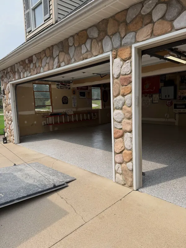 Two-car garage with a stone front, doors open to a finished gray flake floor
