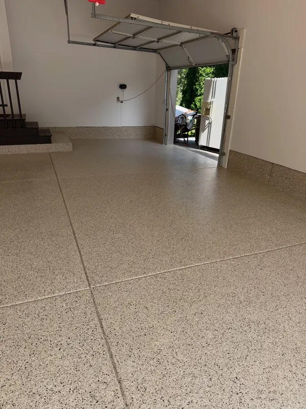 Garage with a tan flake floor coating and black steps leading into the house