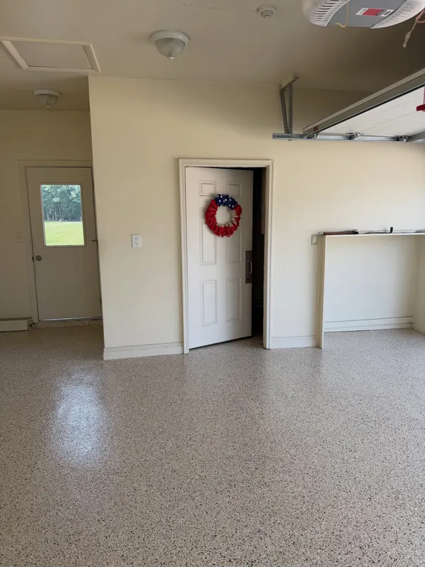 Garage with a tan flake floor, a white door and a window