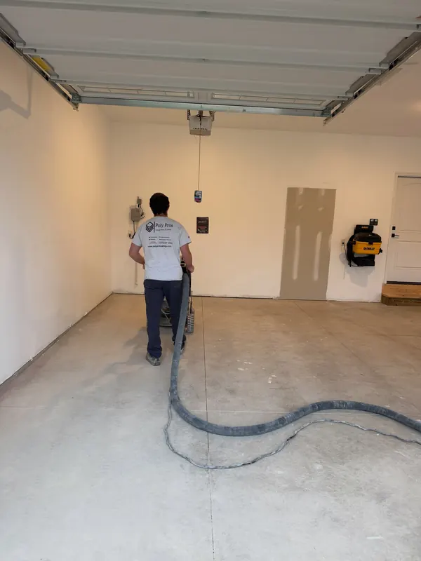 Installer grinding a bare garage slab with a vacuum hose to control dust