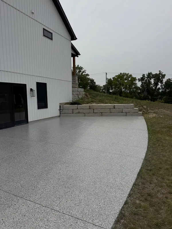 Curved concrete patio coated in a light flake finish beside a white farmhouse with stone steps