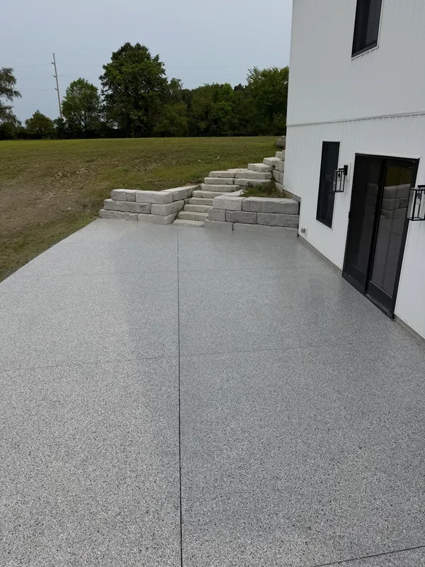 Long coated patio along a white farmhouse-style home with stone steps up the hill