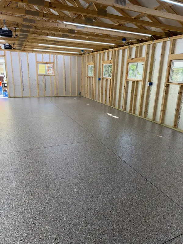 Open pole barn interior with stud walls and a coated gray flake floor under shop lighting