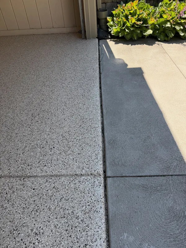 Coated side-entry porch slab meeting bare driveway concrete, with plants along the edge