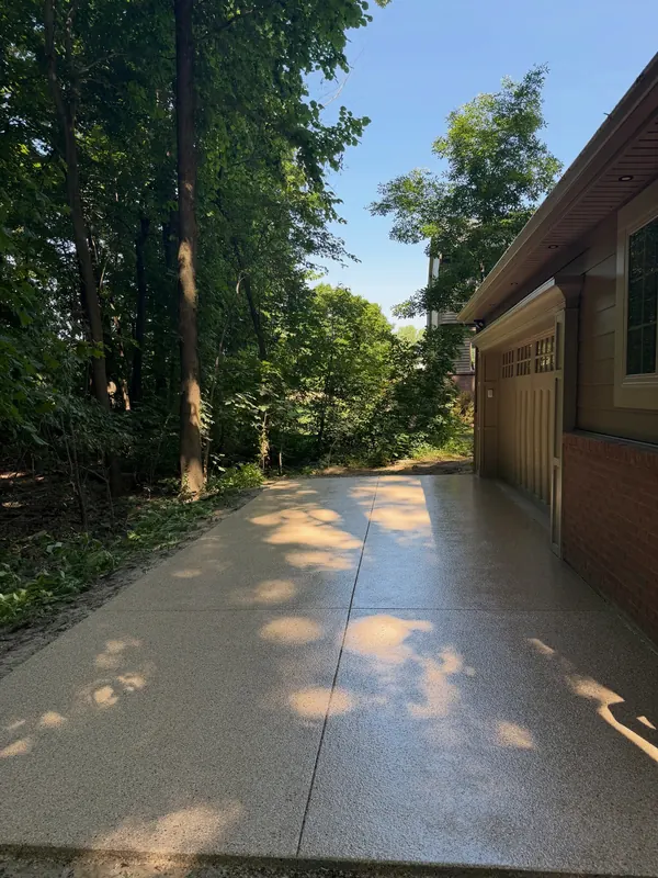 Coated concrete walkway running along a garage beside a wooded lot in summer